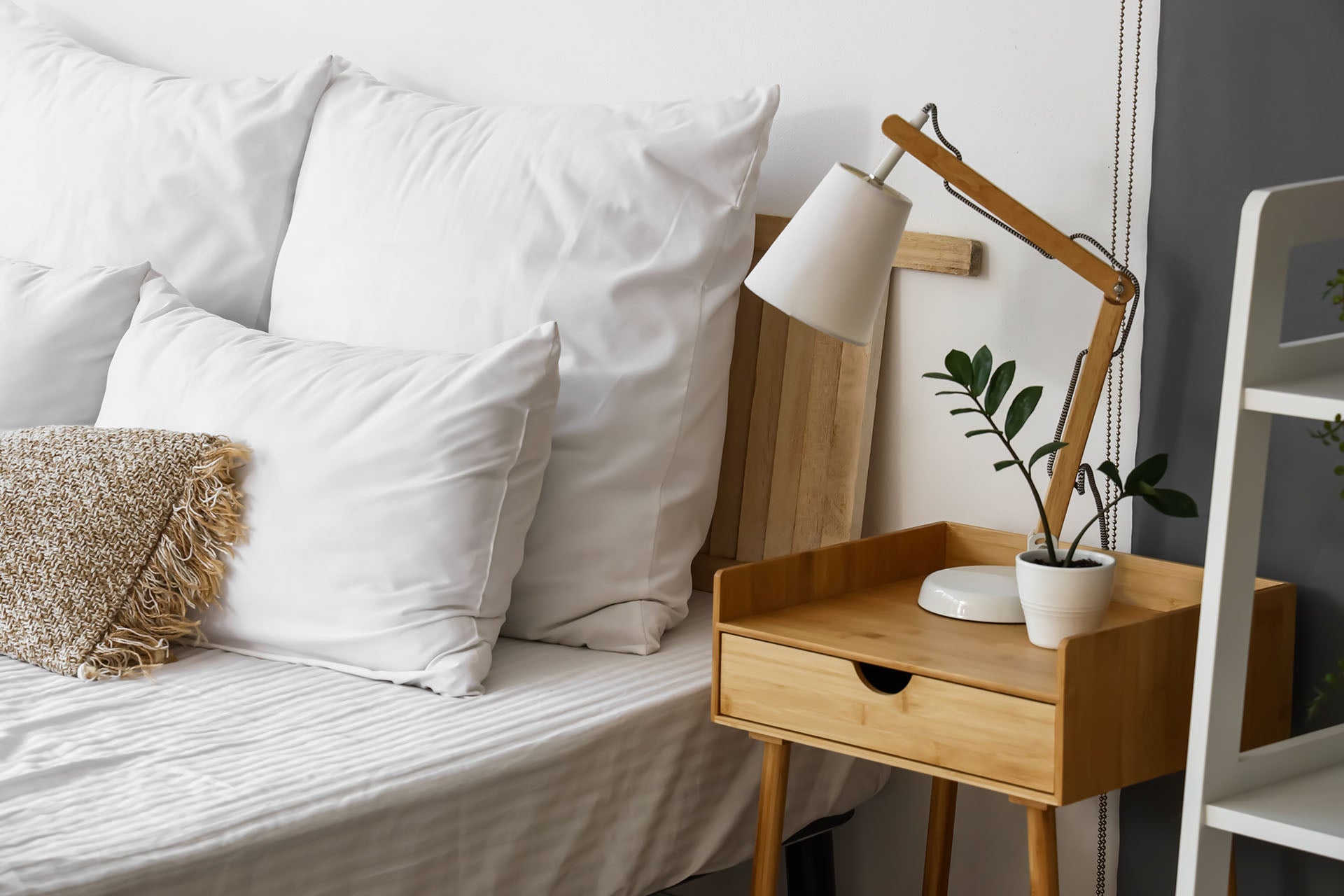 Small wooden bedside table and lamp next to white bed