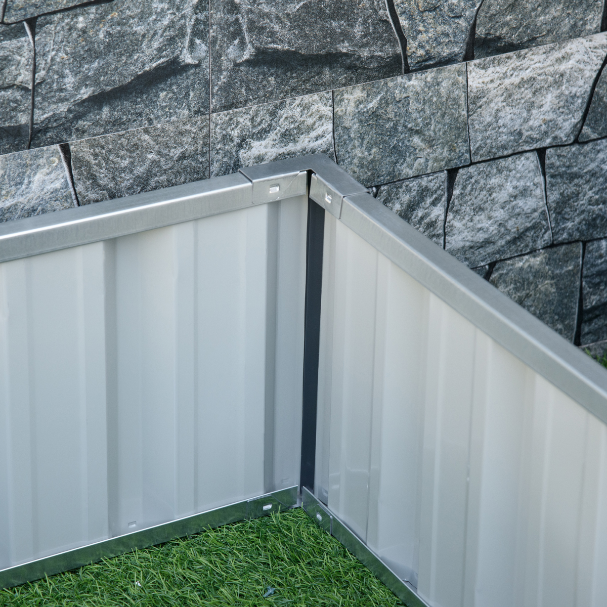 Corner view of a silver metal raised garden bed with rigid panels, 2.58m x 0.9m, near a stone wall.