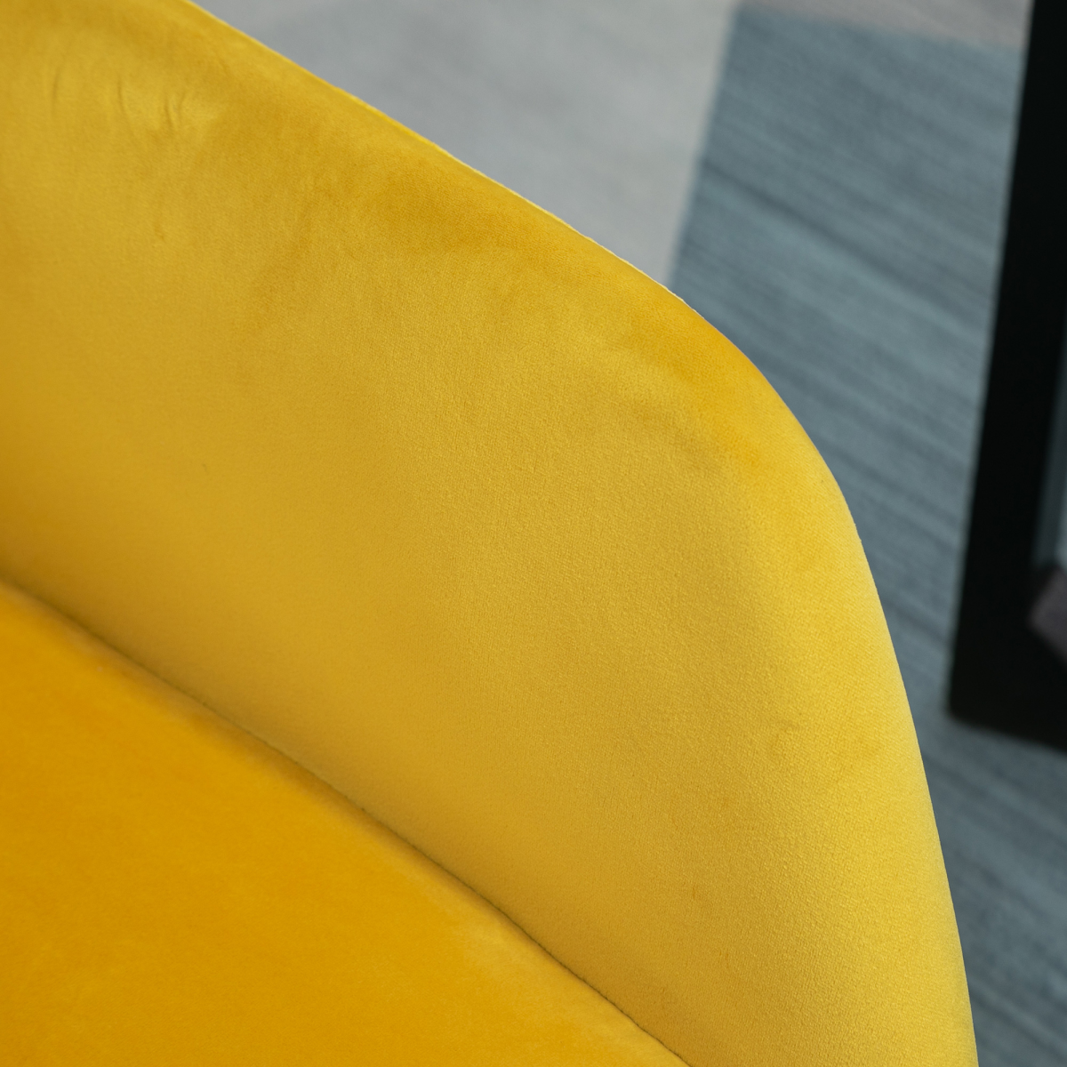 Yellow velvet accent chair close-up showing curved arm and plush upholstery.