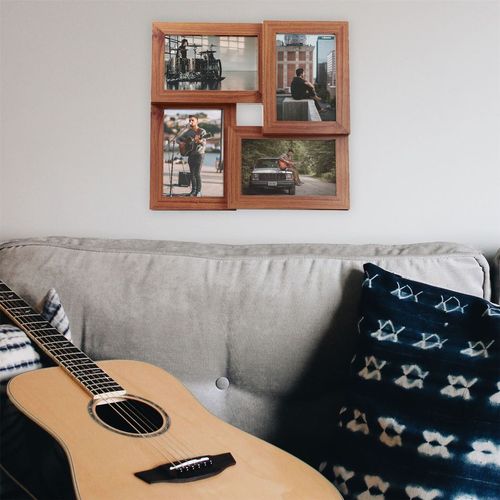A cozy living room showcases a gray couch with patterned pillows and an acoustic guitar on the seat. Above the couch, a Maison & White Multi Picture Aperture Photo Frame with an elegant wood veneer finish displays four 6 x 4 photographs in a collage.