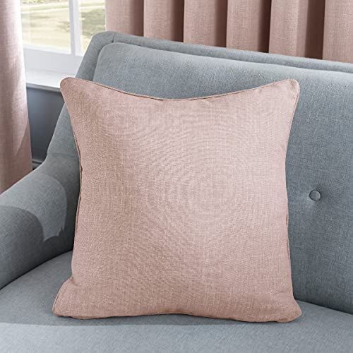 A Sleepdown LINEN LOOK CUSHION BLUSH 45CM adorns a light grey couch. Behind it, beige curtains partially open to reveal a window, creating a cozy living room ambiance.