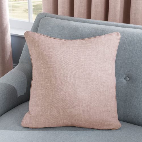 The LINEN LOOK CUSHION BLUSH 45CM by Sleepdown, a square luxury cushion in light pink, adorns a gray couch. Beige curtains frame the partially visible window as natural light enhances the cushions textured fabric.