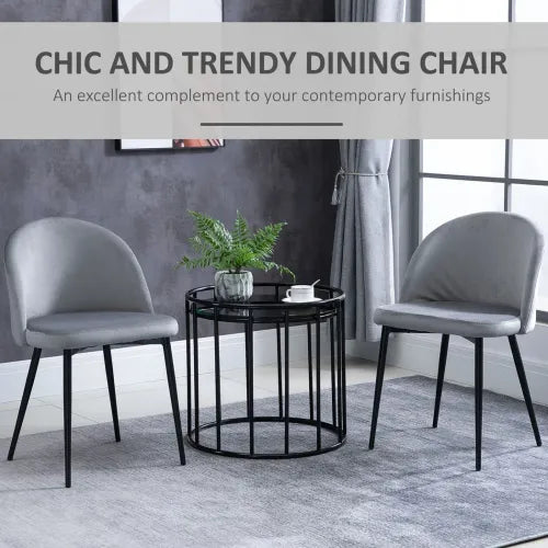 Two Unbranded dining chairs, 2 Pieces Modern Upholstered Fabric Bucket Seat Dining Chairs Living Room Grey, with velvet-feel grey upholstery and sleek design, flank a round black table topped with a plant. The modern setting features grey walls, matching curtains, and a stylish rug.
