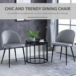 Two Unbranded dining chairs, 2 Pieces Modern Upholstered Fabric Bucket Seat Dining Chairs Living Room Grey, with velvet-feel grey upholstery and sleek design, flank a round black table topped with a plant. The modern setting features grey walls, matching curtains, and a stylish rug.