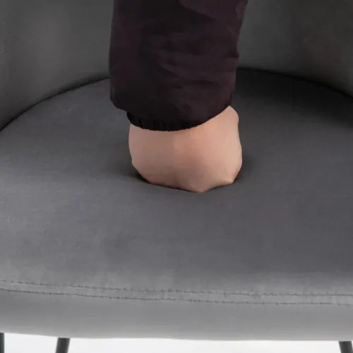 A hand in a black sleeve presses down on the soft cushion of the 2 Pieces Modern Upholstered Fabric Bucket Seat Dining Chairs Living Room Grey by Unbranded, creating an indentation. The armless design and velvet-feel upholstery enhance comfort and pliability, subtly supported by a sturdy steel frame.