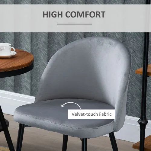 A High Comfort label leads to an arrow pointing at the 2-piece Modern Upholstered Fabric Bucket Seat Dining Chairs in grey, sitting beside a round wooden table with a white teacup. The curved backrest of the chair features Velvet-touch Fabric. Textured wallpaper enhances the background.